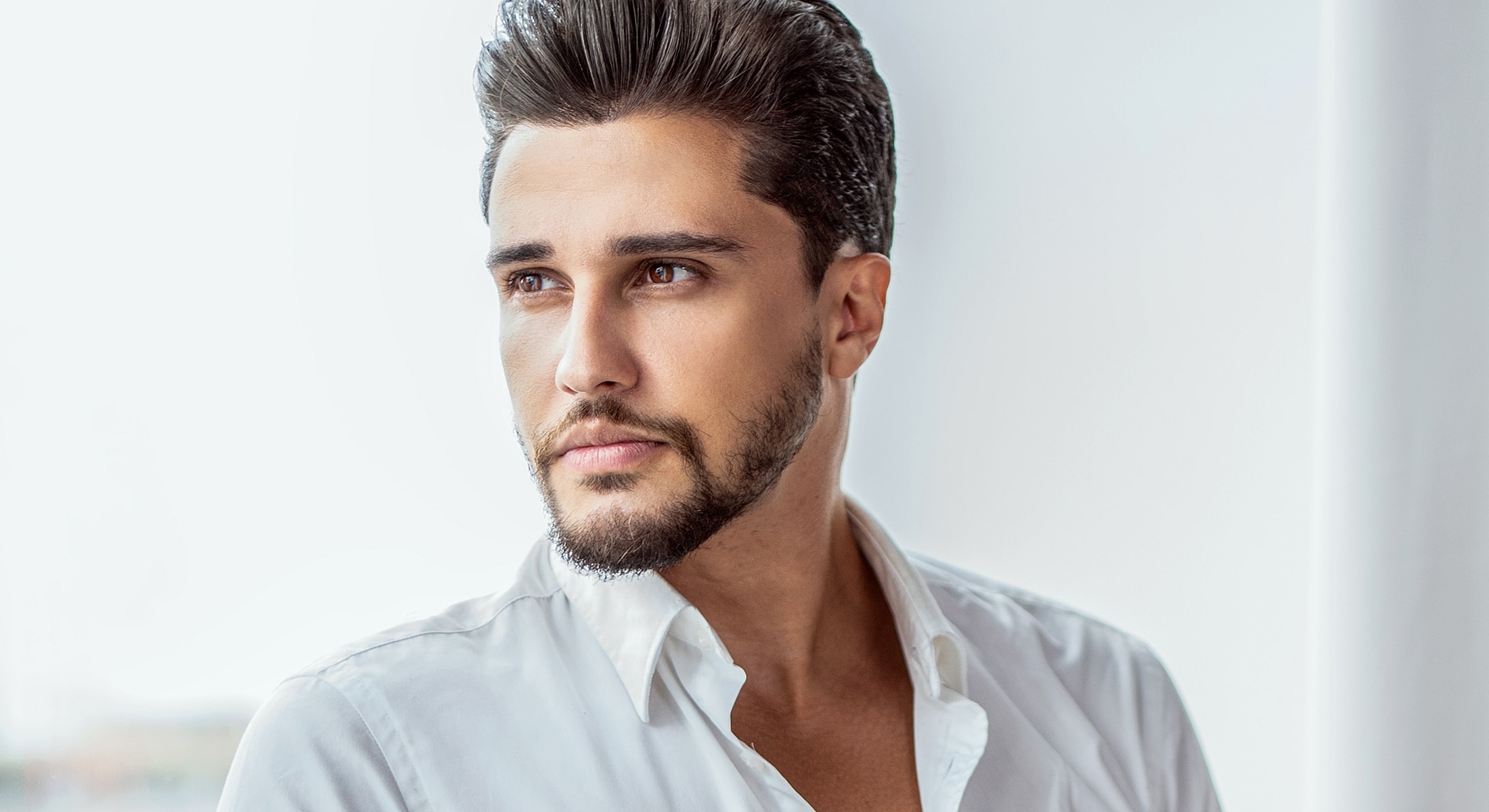 Man in white shirt gazing thoughtfully out window.